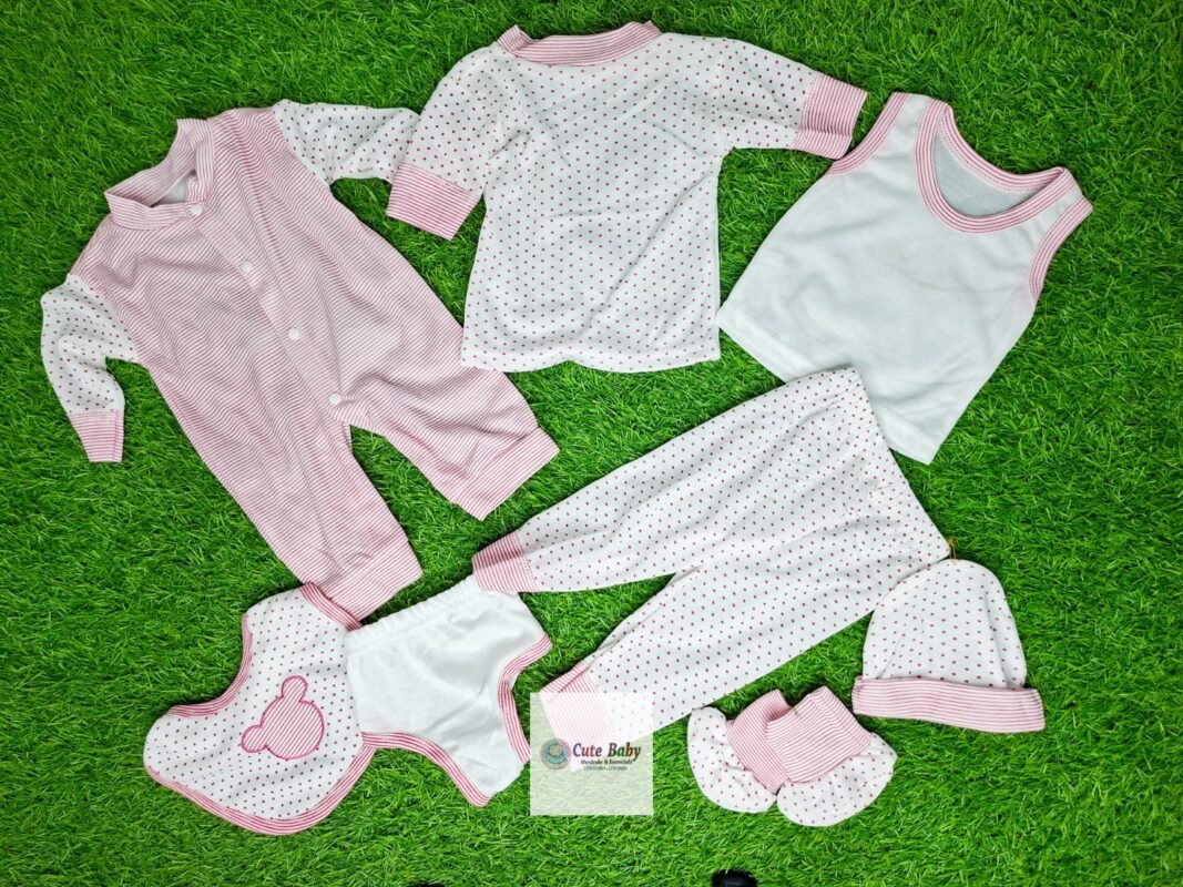 Pink and white eight-piece baby clothing gift set laid out on a green background