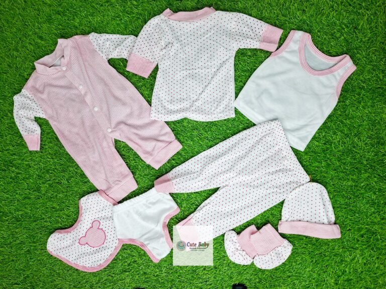 Pink and white eight-piece baby clothing gift set laid out on a green background